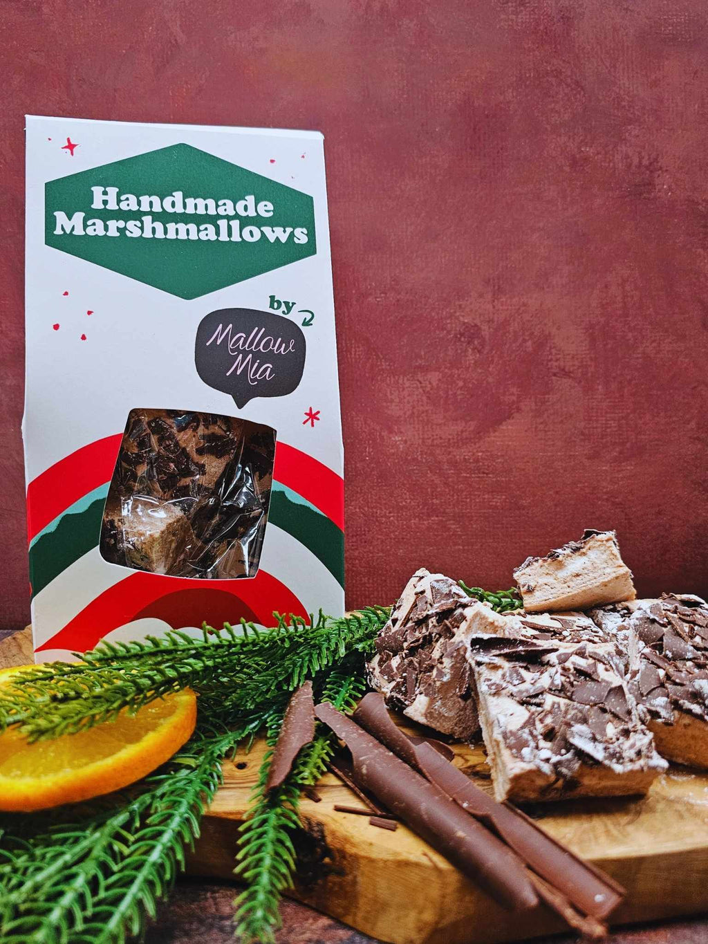 Handmade marshmallows with packaging and garnishes on a wooden board against a red background