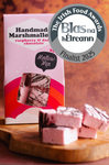 Handmade raspberry marshmallow with chocolate drizzle on a wooden board with 'Blas na hEireann' award badge.